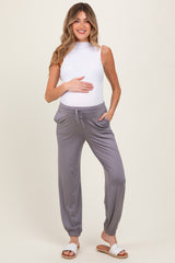 woman wearing a white sleeveless top and gray maternity jogger pants, holding her baby bump