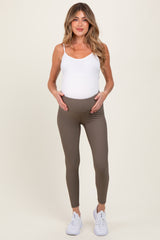 woman wearing a white maternity tank top and brown ribbed maternity leggings, holding her baby bump