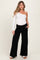 woman wearing a white one-shoulder maternity top and black wide-leg pants, showing off her baby bump