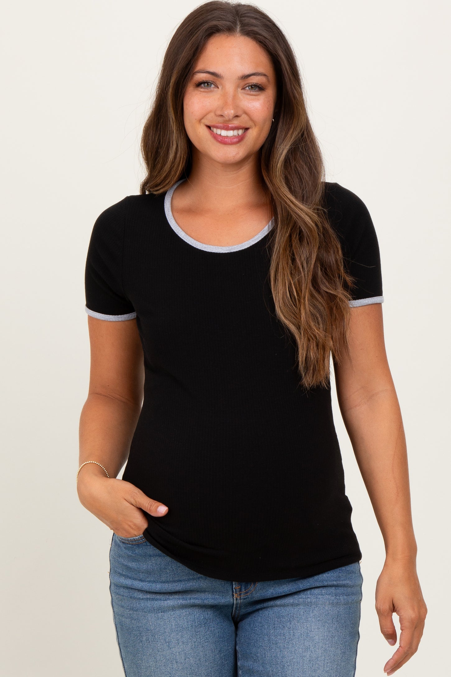 woman wearing a black maternity top with contrasting gray trim and short sleeves, smiling and posing with a baby bump visible