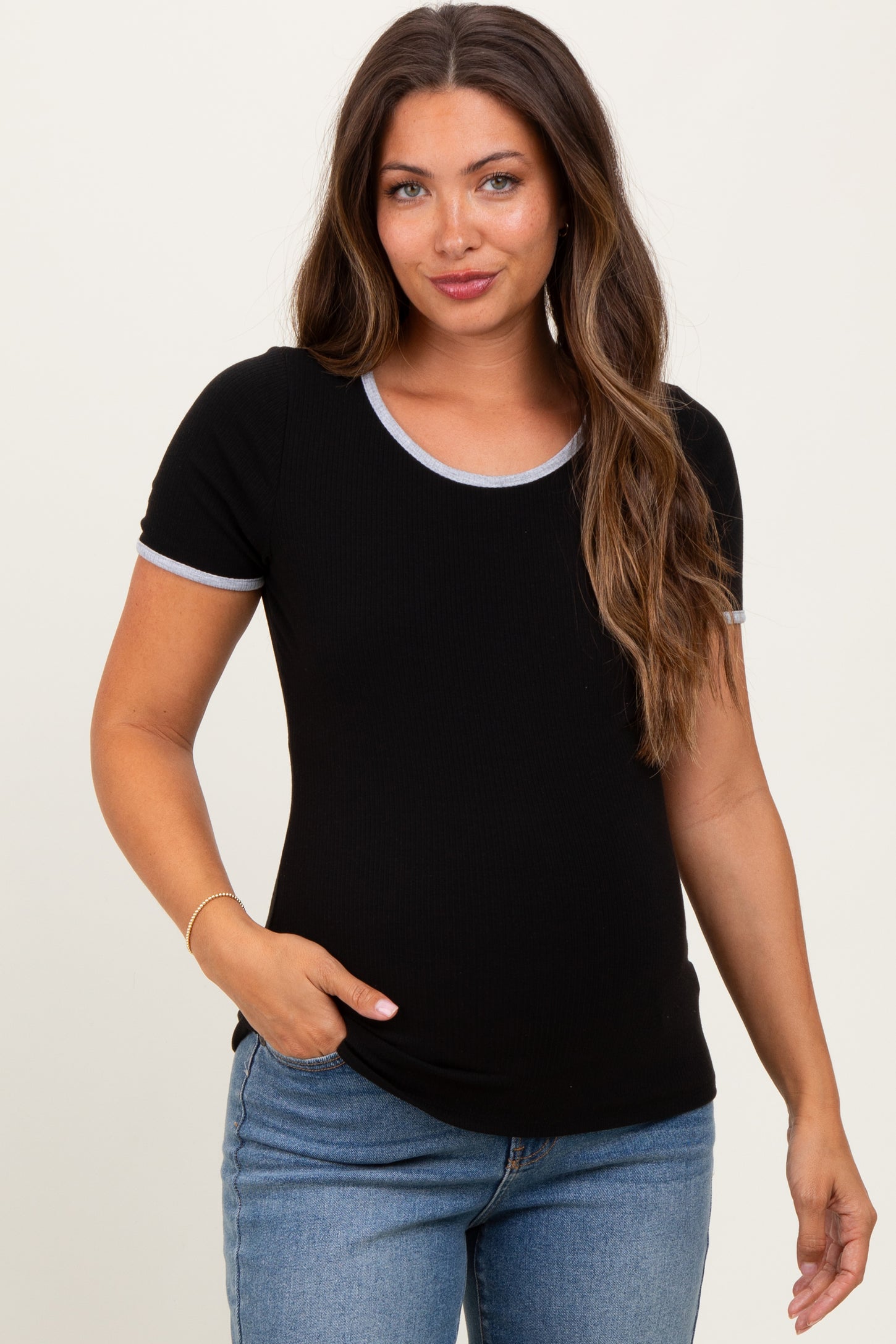 woman wearing a black maternity top with short sleeves and light blue trim, posing with a hand in her pocket