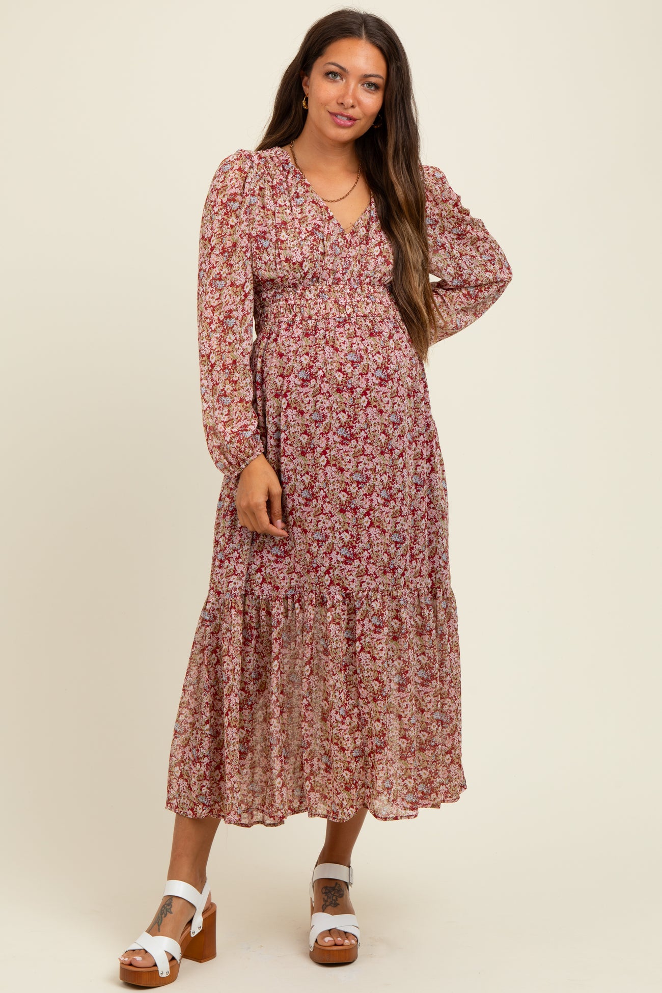 woman wearing a floral long sleeve maternity dress with a tiered skirt and a v-neckline, posing against a neutral background