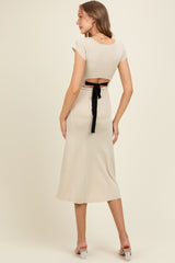 woman wearing a beige maternity dress with cap sleeves and a tie-back detail, showing a visible baby bump