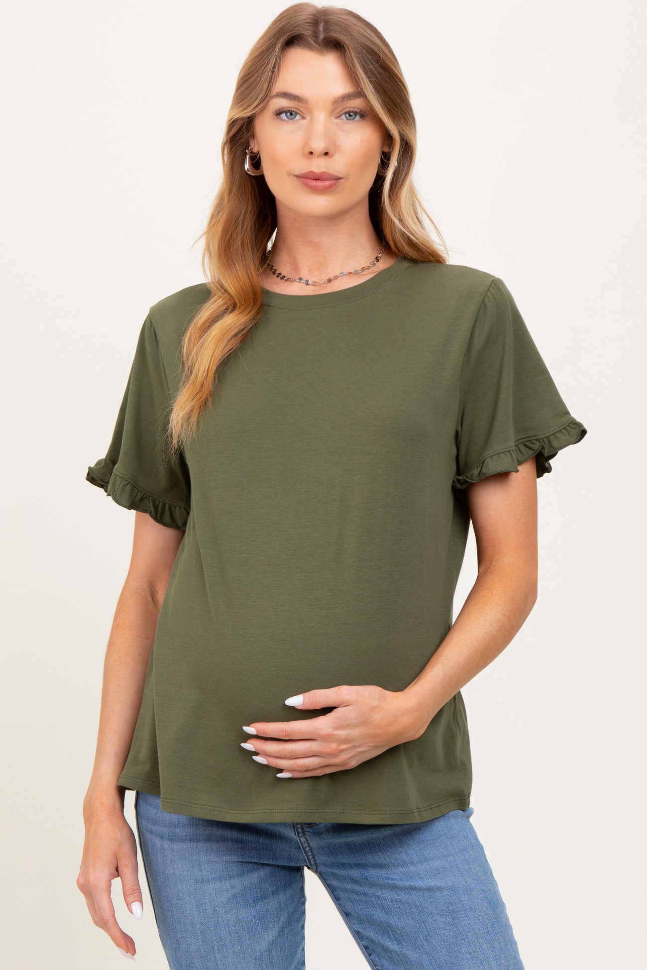 woman wearing a dark green maternity top with ruffled sleeves and holding her baby bump