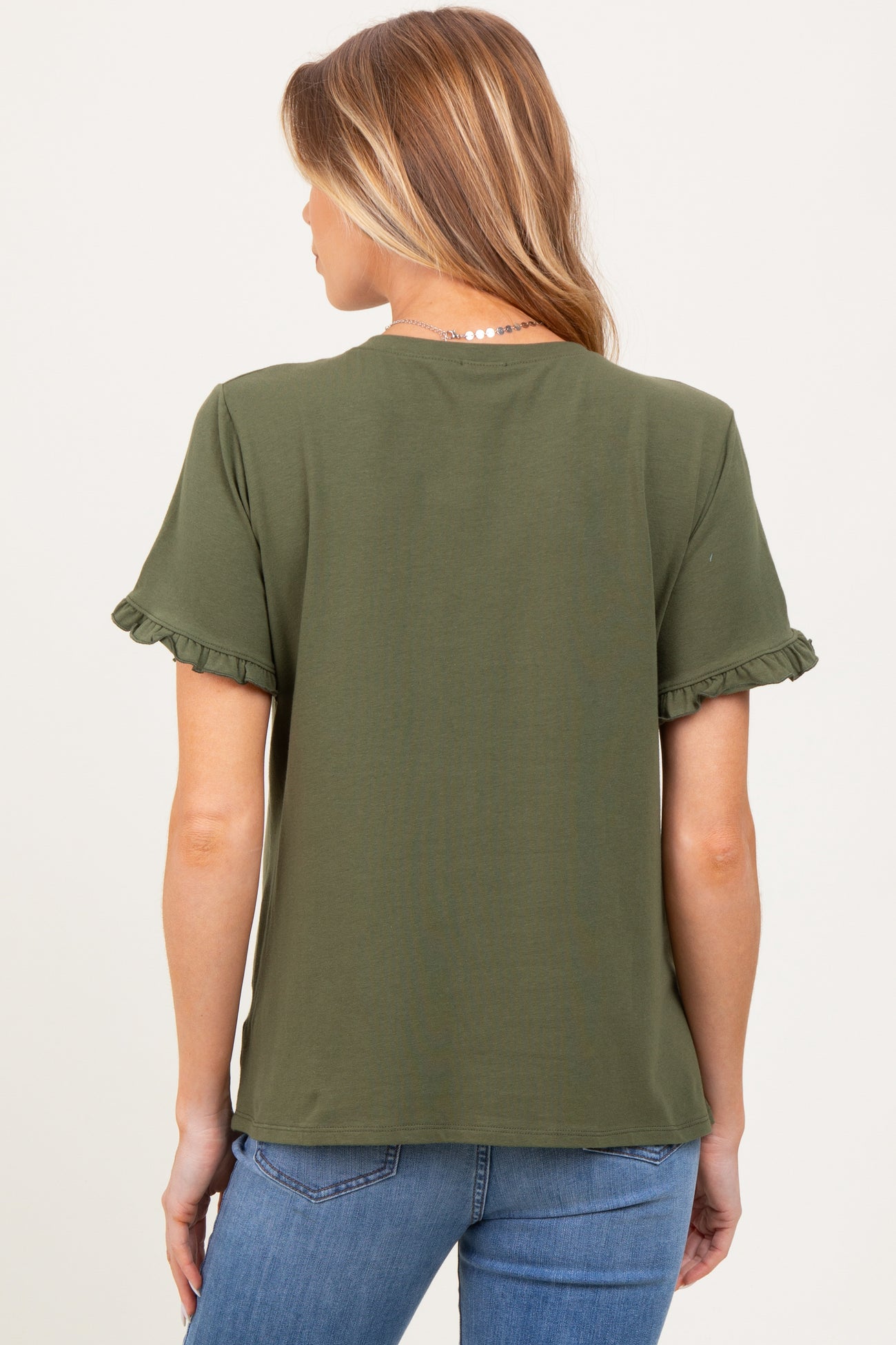 woman wearing an olive green maternity top with ruffled sleeves, shown from the back, paired with blue jeans