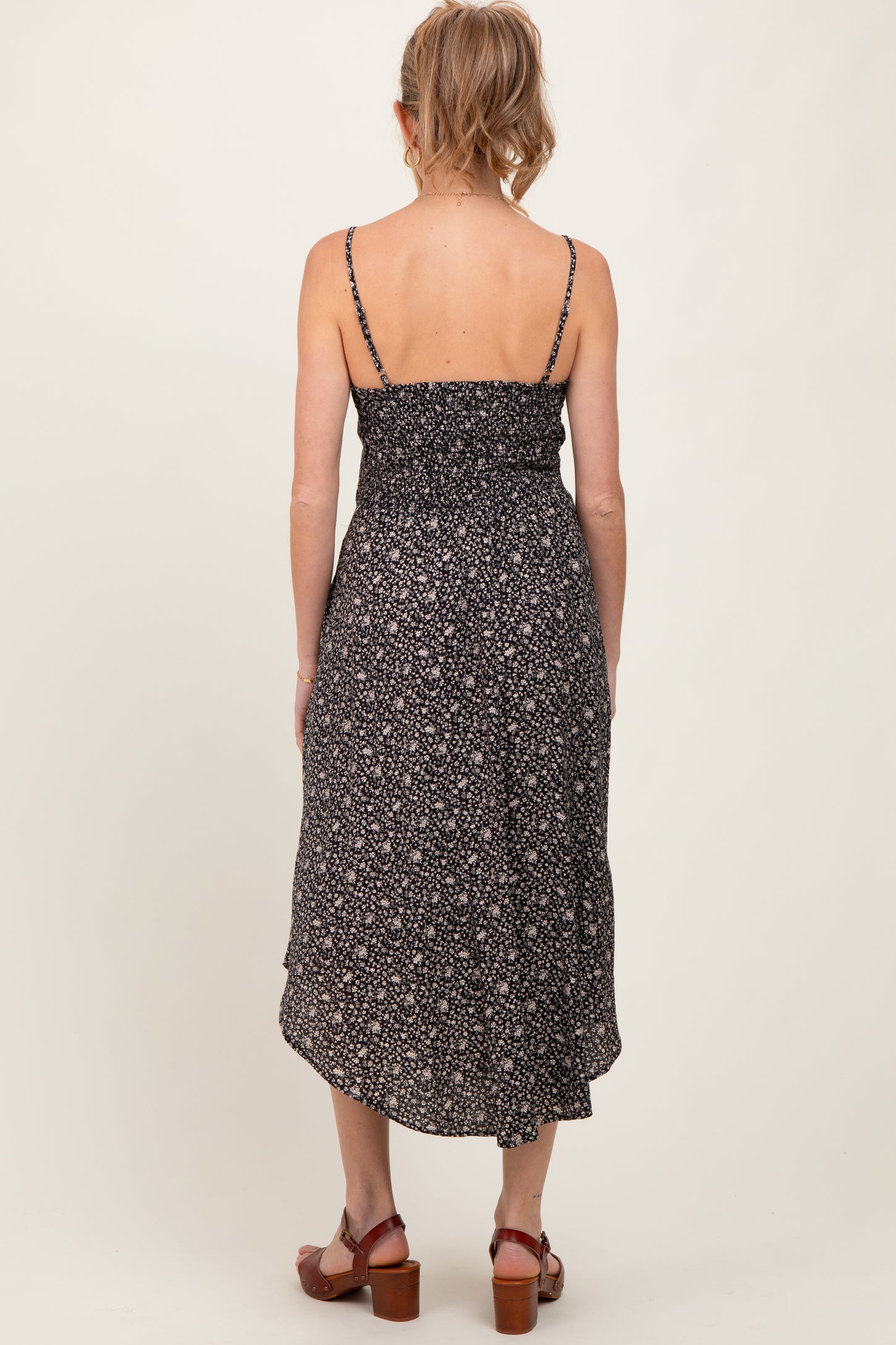 woman wearing a black floral maternity dress with adjustable spaghetti straps and a shirred back, showing a flowing hemline