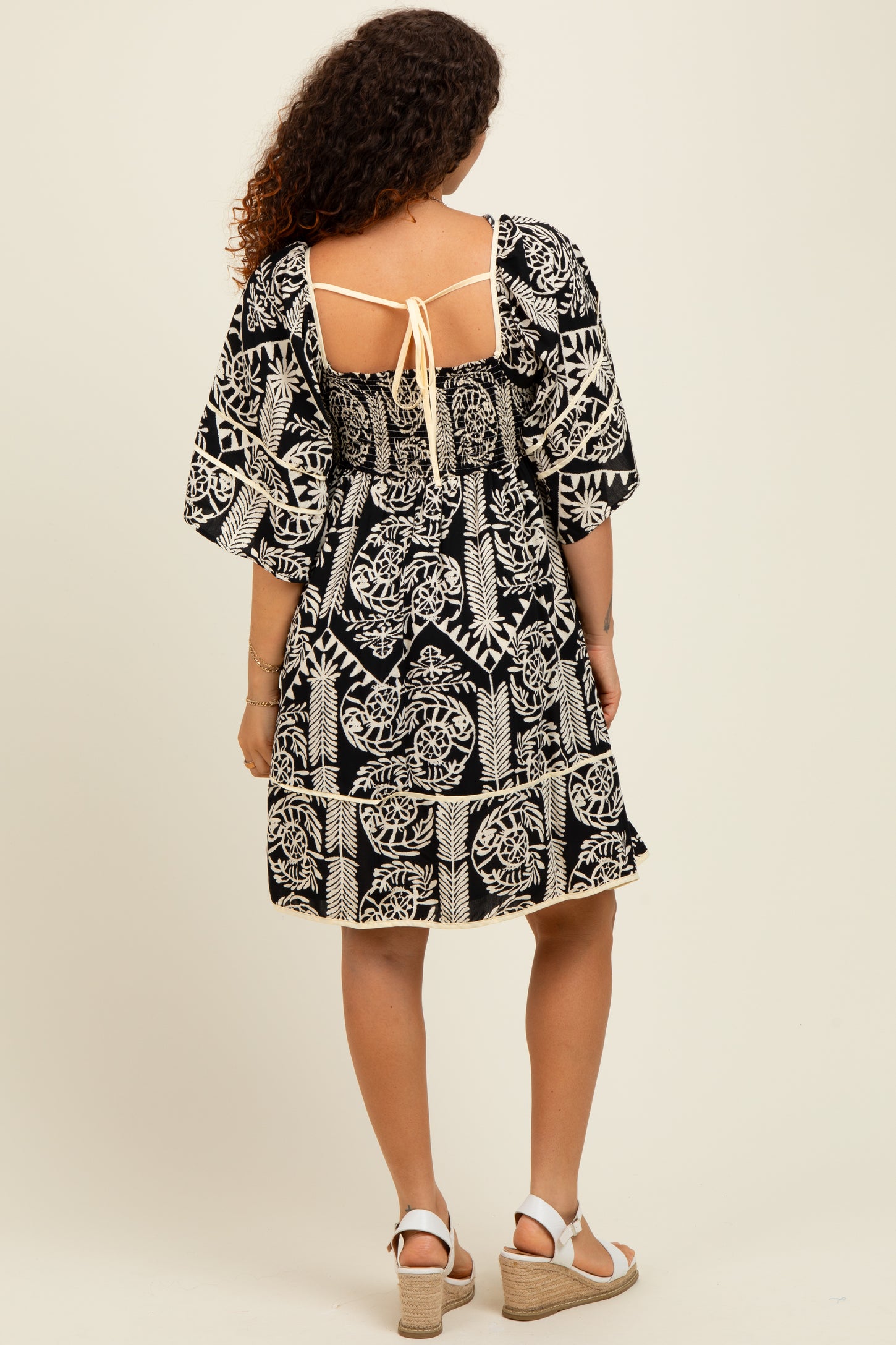woman wearing a black and cream patterned maternity dress with puff sleeves and back tie detail, showing her baby bump