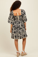 woman wearing a black and cream patterned maternity dress with puff sleeves and back tie detail, showing her baby bump