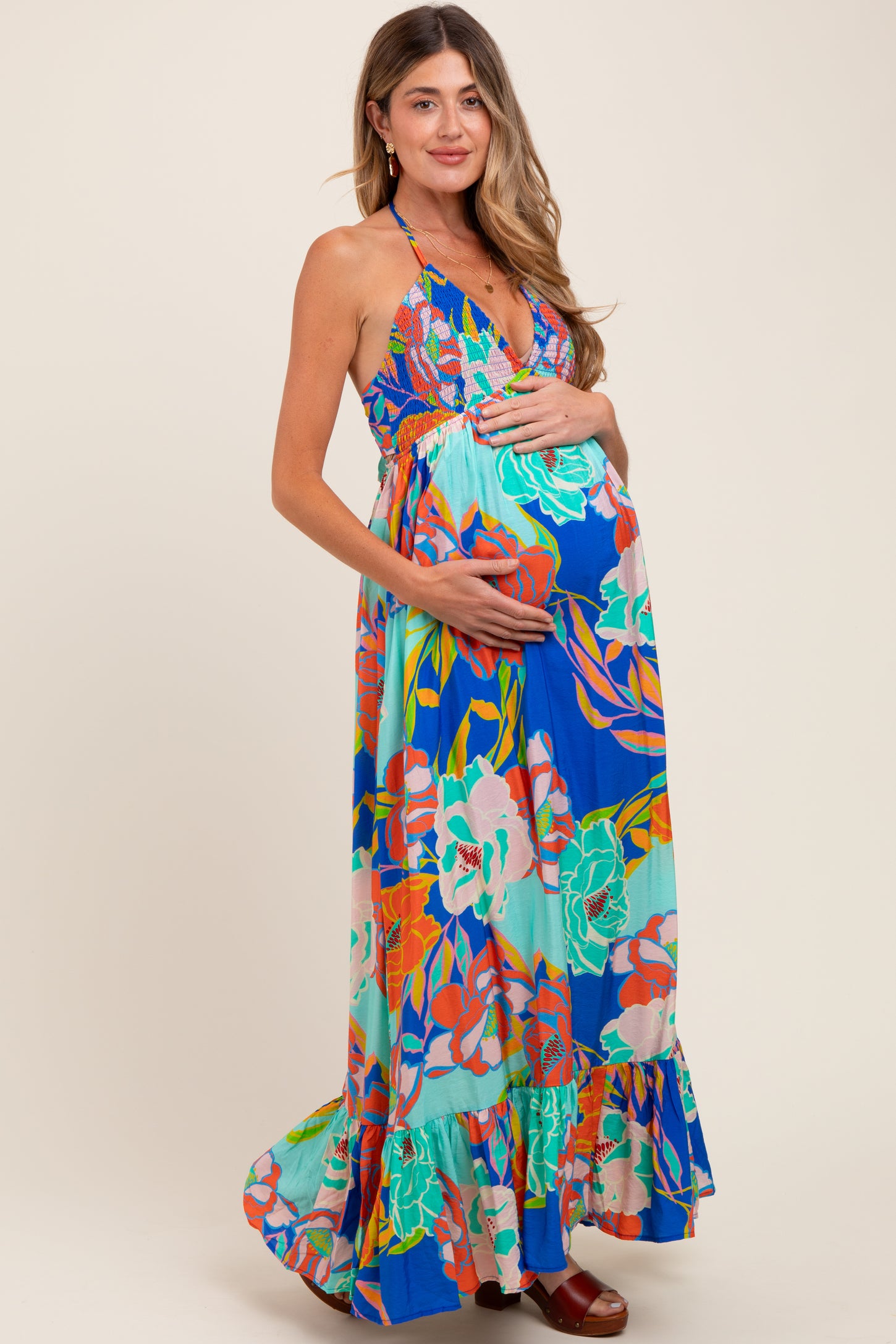 woman wearing a colorful floral maternity maxi dress and cradling her baby bump