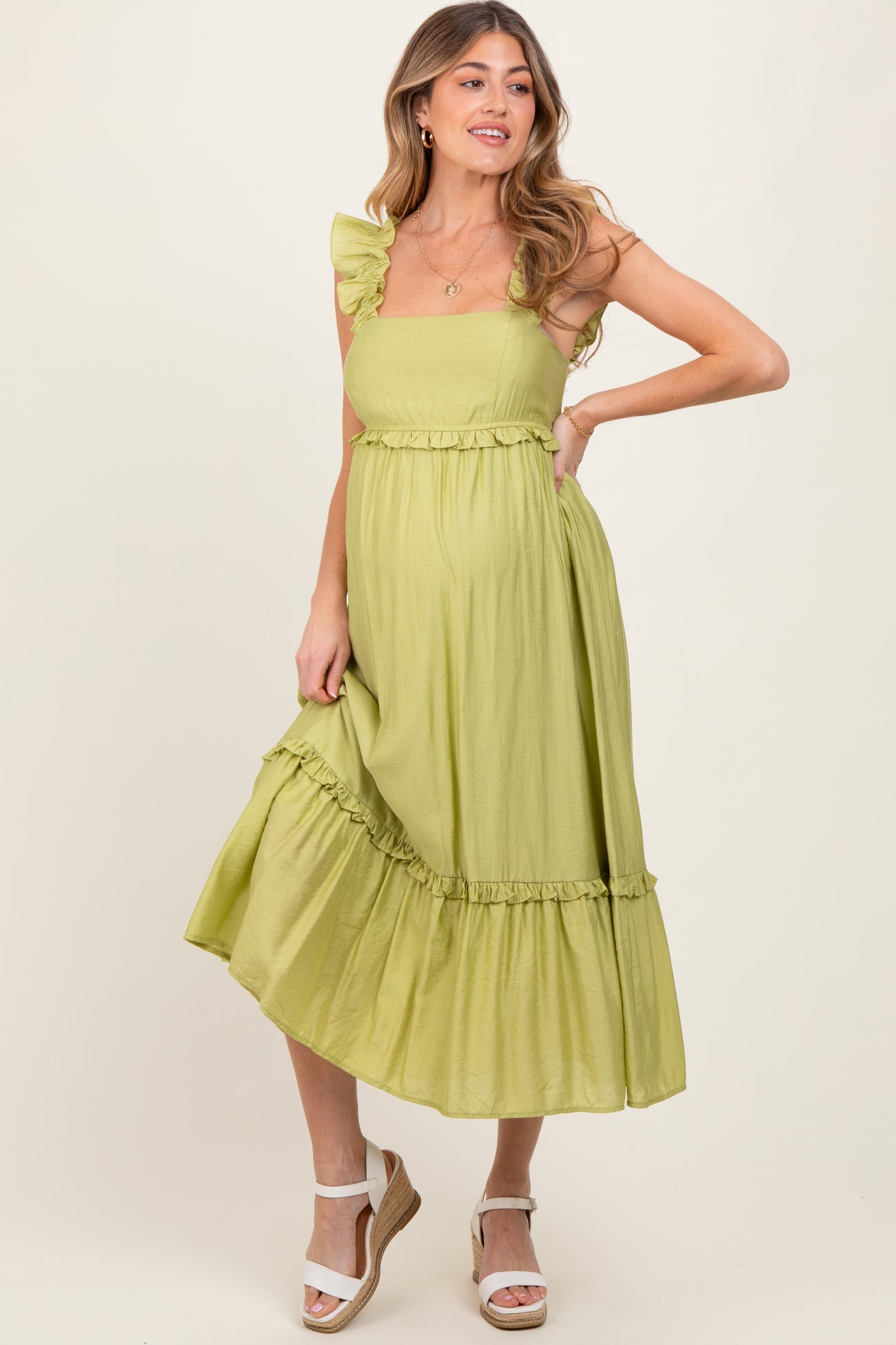 woman wearing a light green maternity dress with ruffle straps and a tiered skirt, showing a baby bump