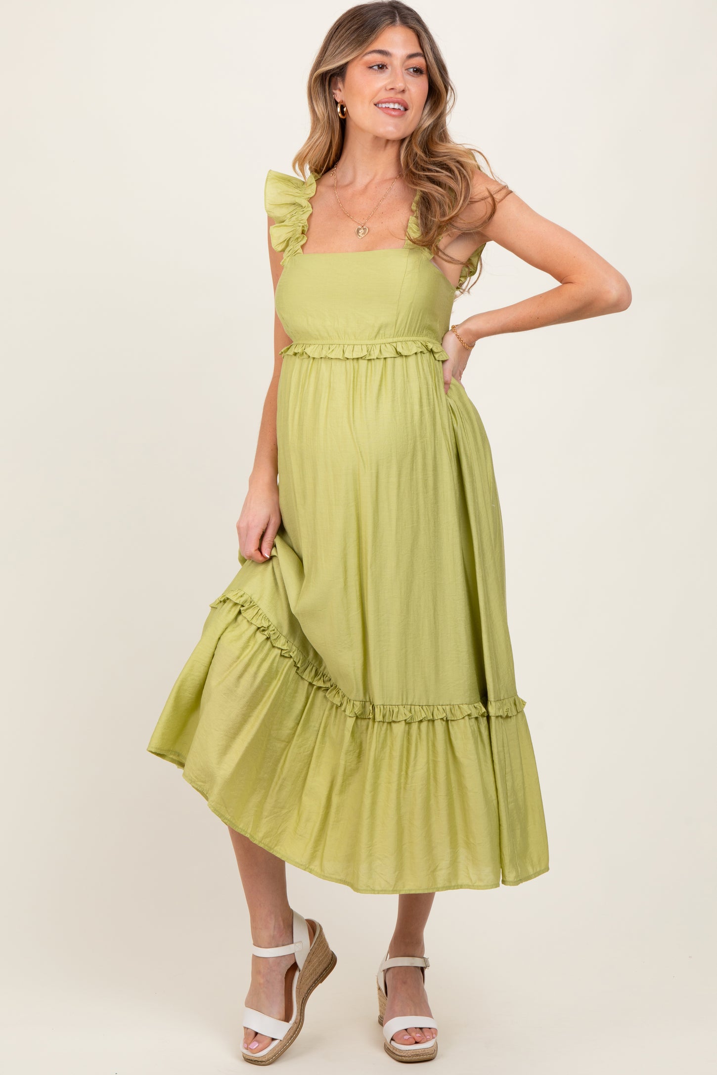 woman wearing a light green maternity dress with ruffle straps and a tiered skirt, showing a baby bump