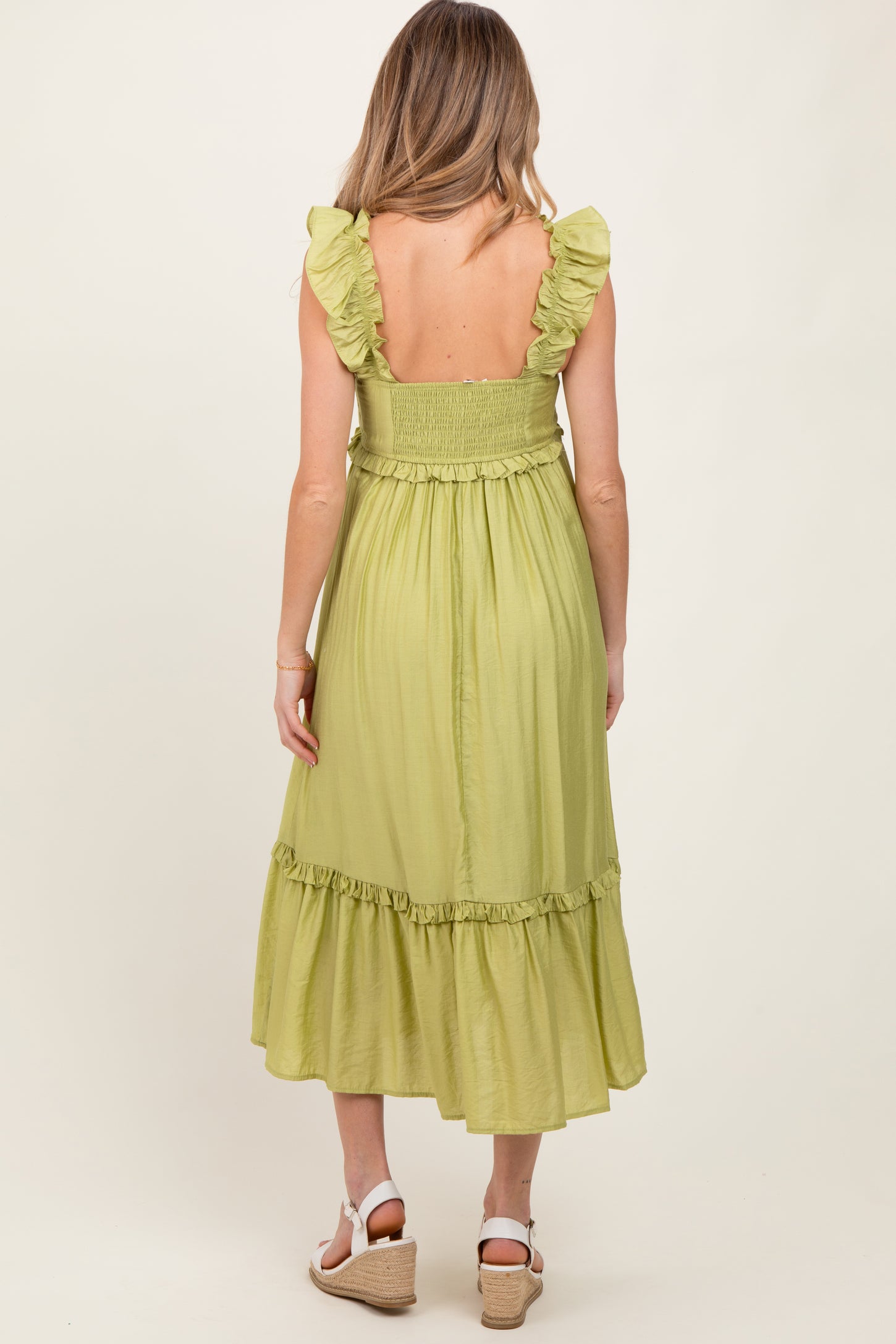 woman wearing a light green maternity dress with ruffled straps and a tiered skirt, showing her back