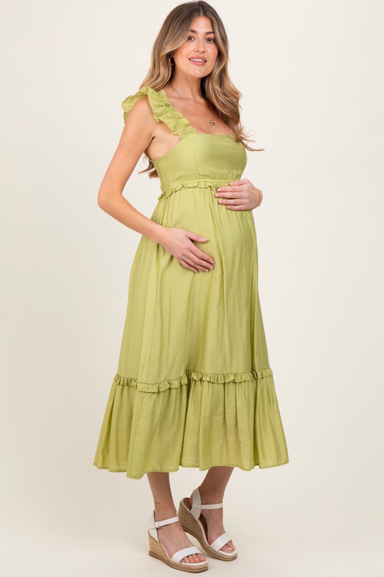 woman wearing a light green maternity dress with ruffled straps and a tiered hem, holding her baby bump