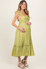 woman wearing a light green maternity dress with ruffled straps and a tiered hem, holding her baby bump