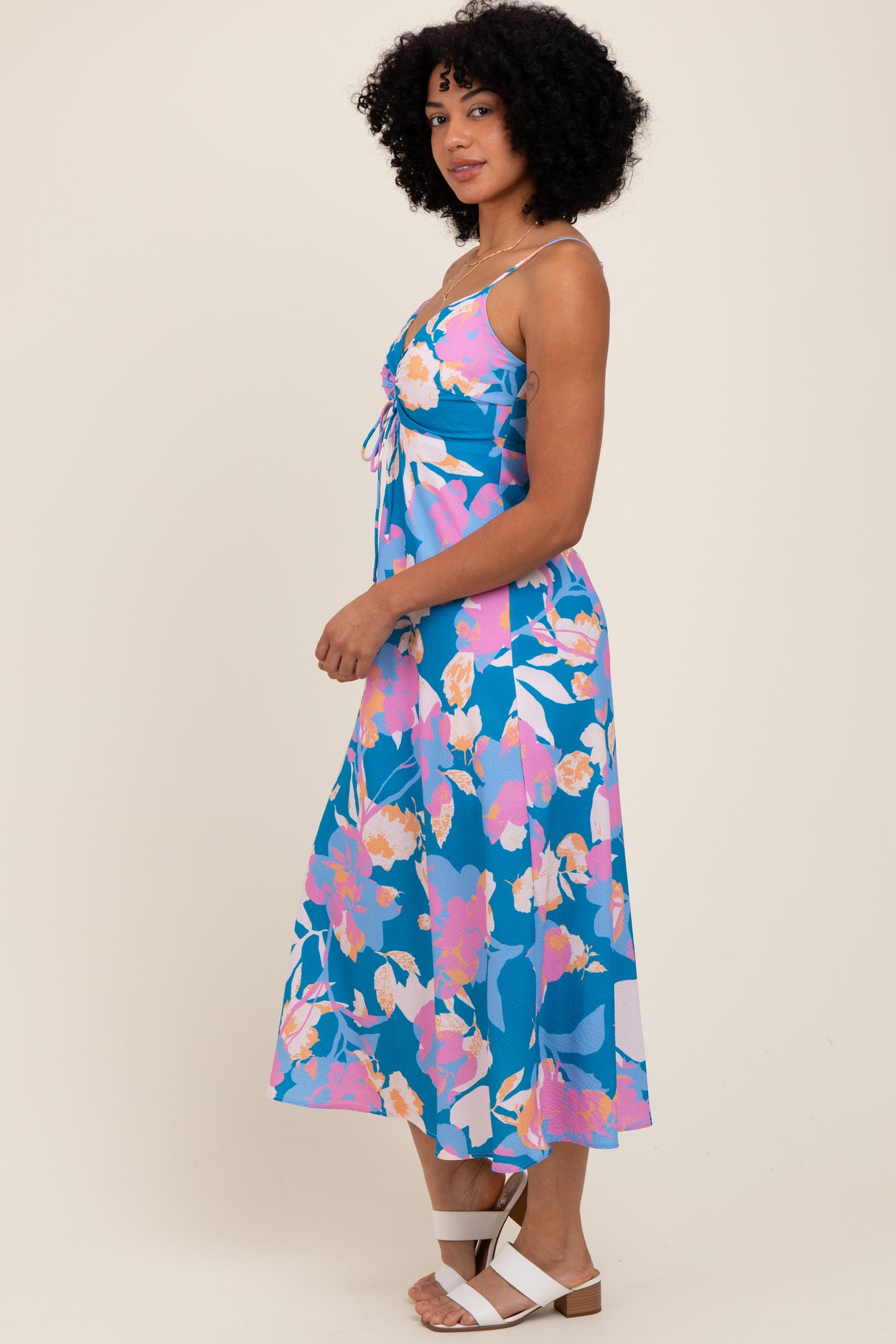 woman wearing a blue floral maxi dress with a tie detail and spaghetti straps, styled with white sandals