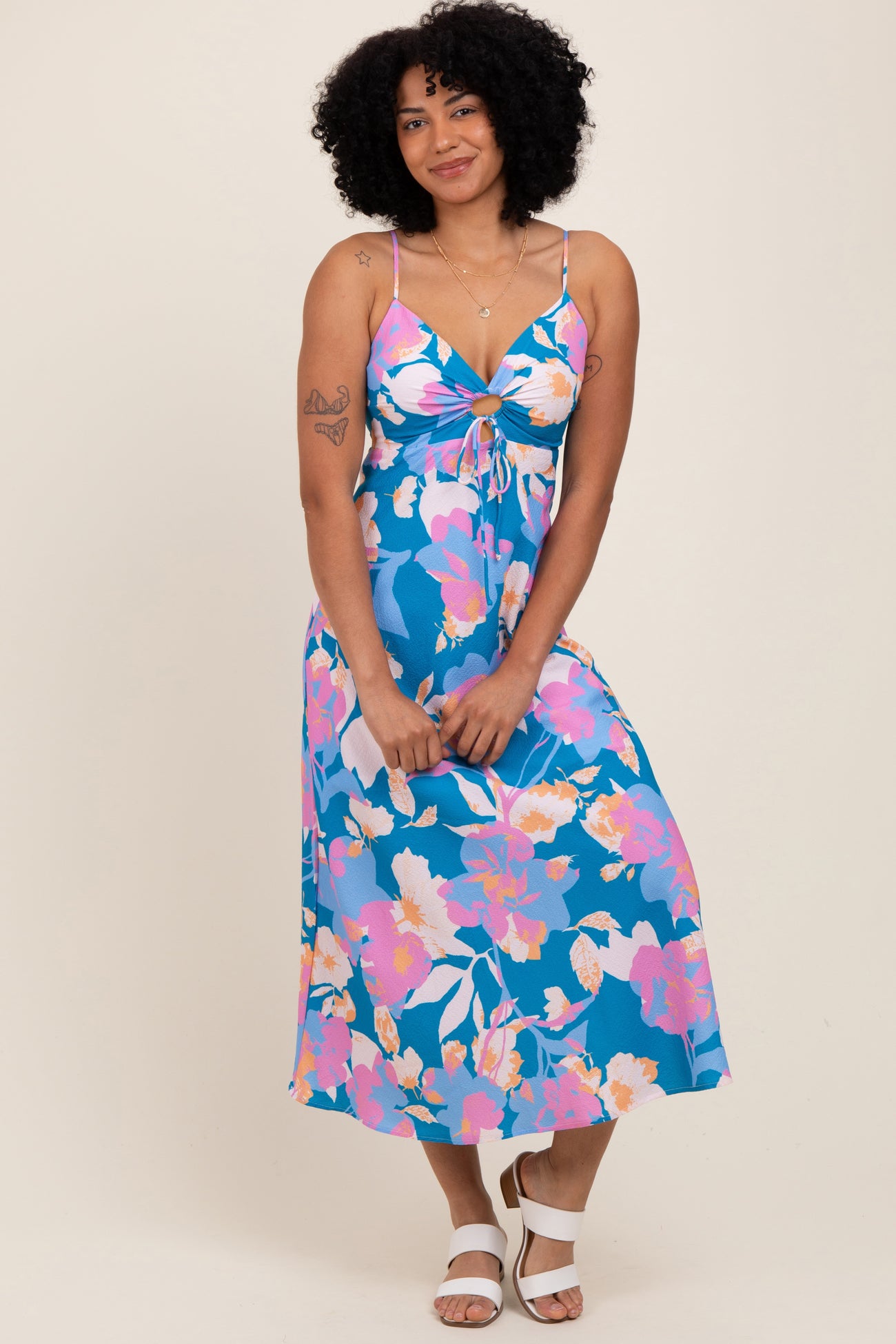 woman wearing a blue floral midi dress with a tie front and spaghetti straps, standing against a neutral background