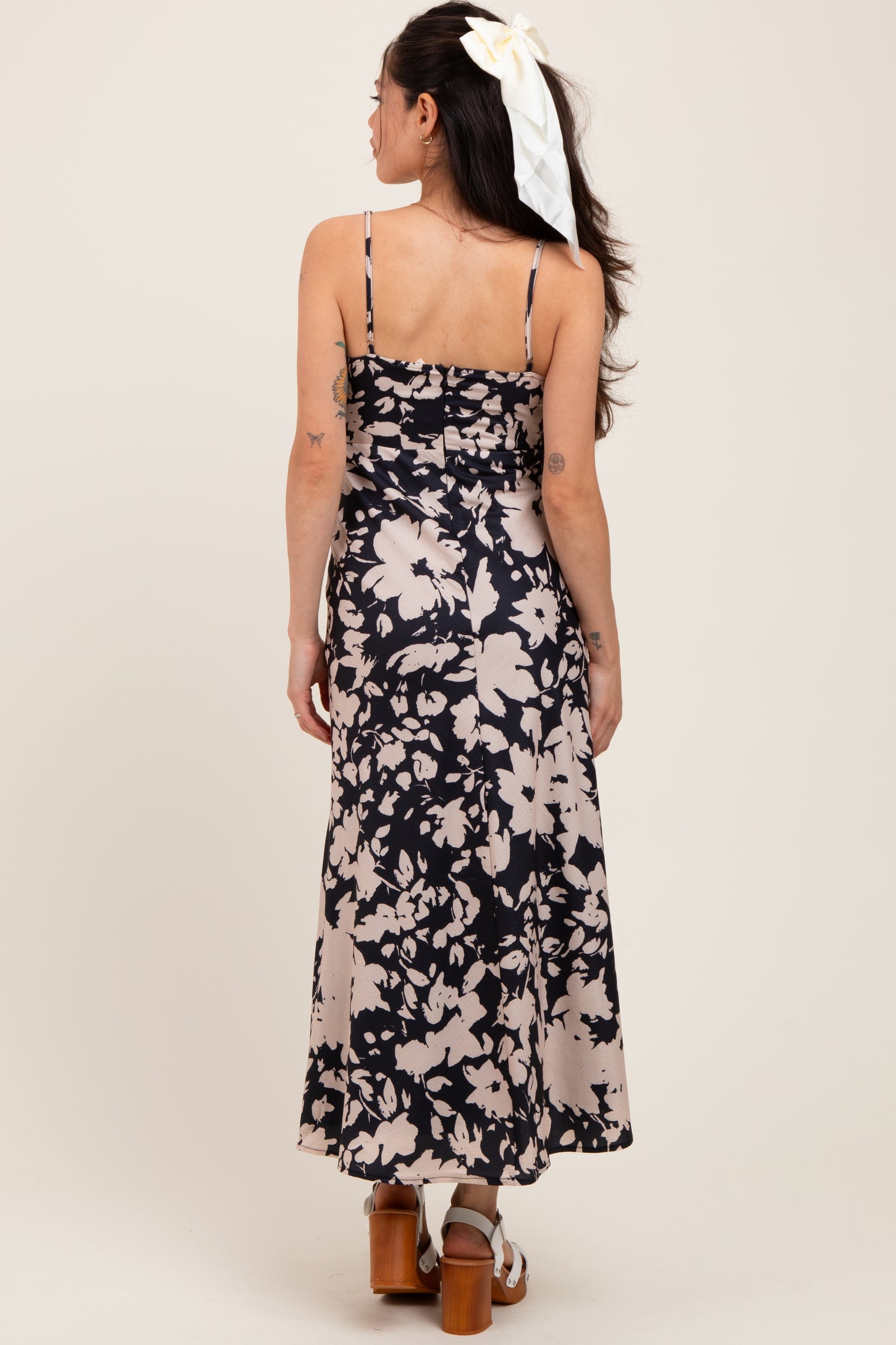 woman wearing a black and beige floral print maternity dress with adjustable straps and a relaxed fit, back view