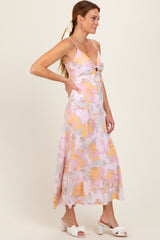 woman wearing a pink floral midi dress with a tie detail at the bust and white heeled sandals