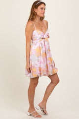 woman wearing a pink floral mini dress with a tie front and thin straps, styled with white sandals and a headband