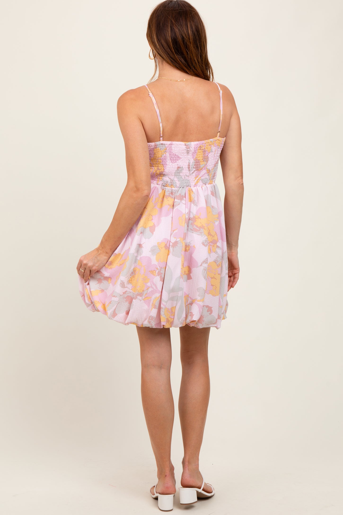woman wearing a floral pink and yellow sundress with a fitted bodice and flared skirt, showing the back view