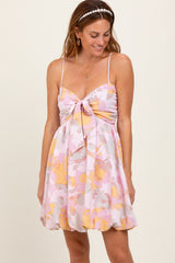woman wearing a pink floral mini dress with a tie front and spaghetti straps