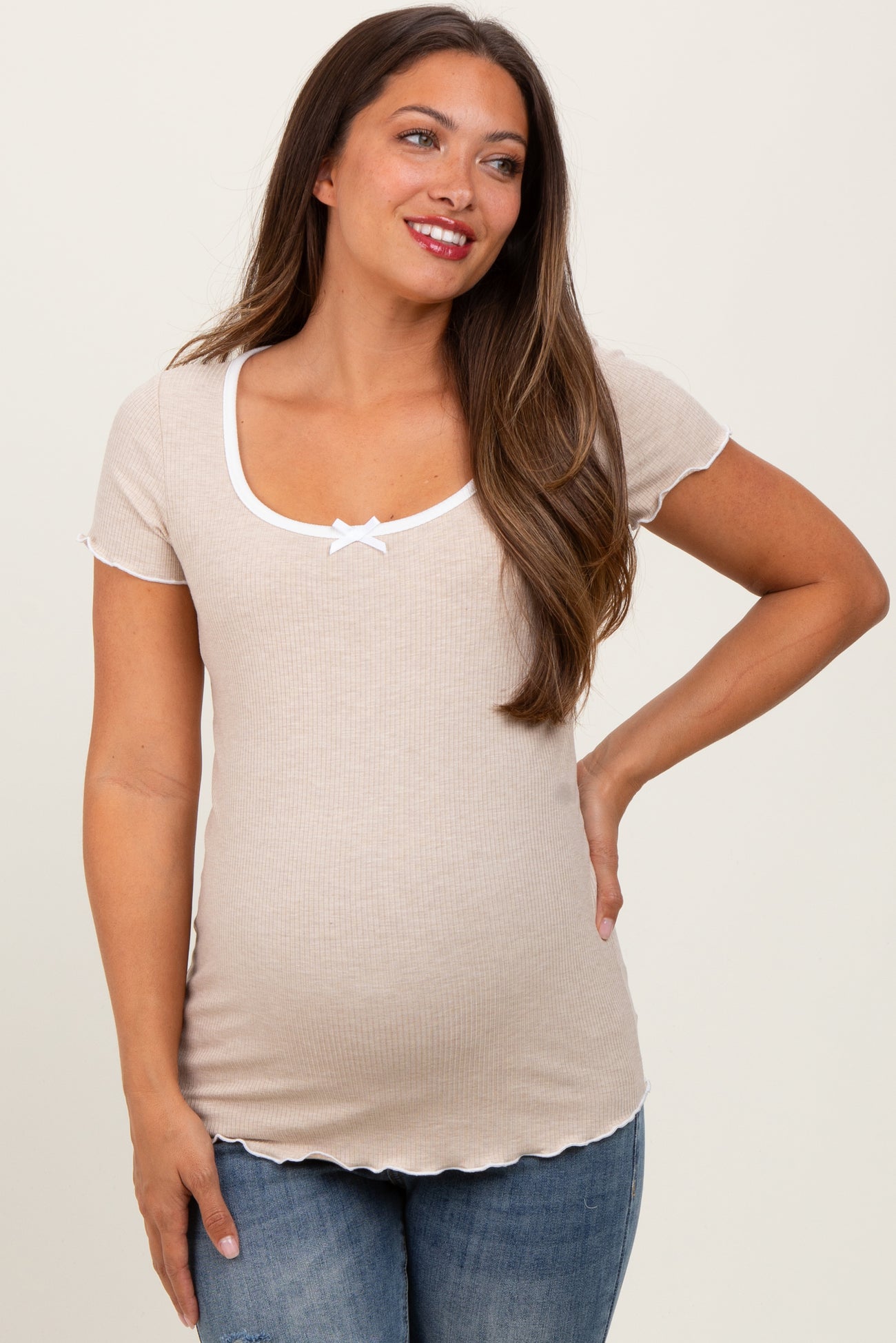 woman wearing a beige short sleeve maternity top with a scoop neck and white bow detail, showing her baby bump