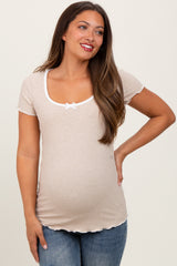 woman wearing a beige short sleeve maternity top with a scoop neck and white bow detail, showing her baby bump