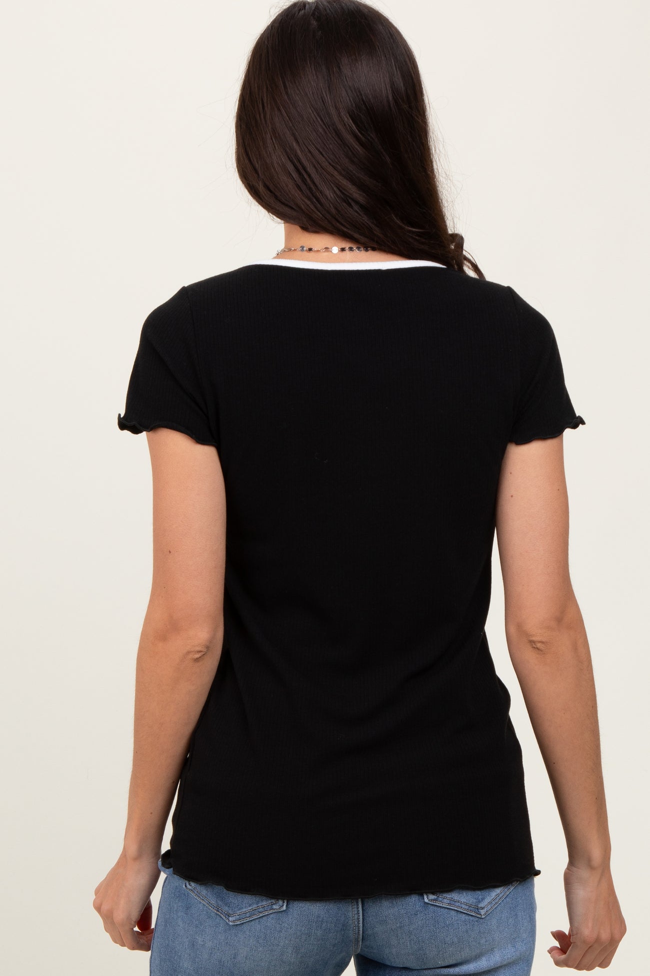 woman wearing a black ribbed short sleeve top, viewed from the back, paired with light blue jeans