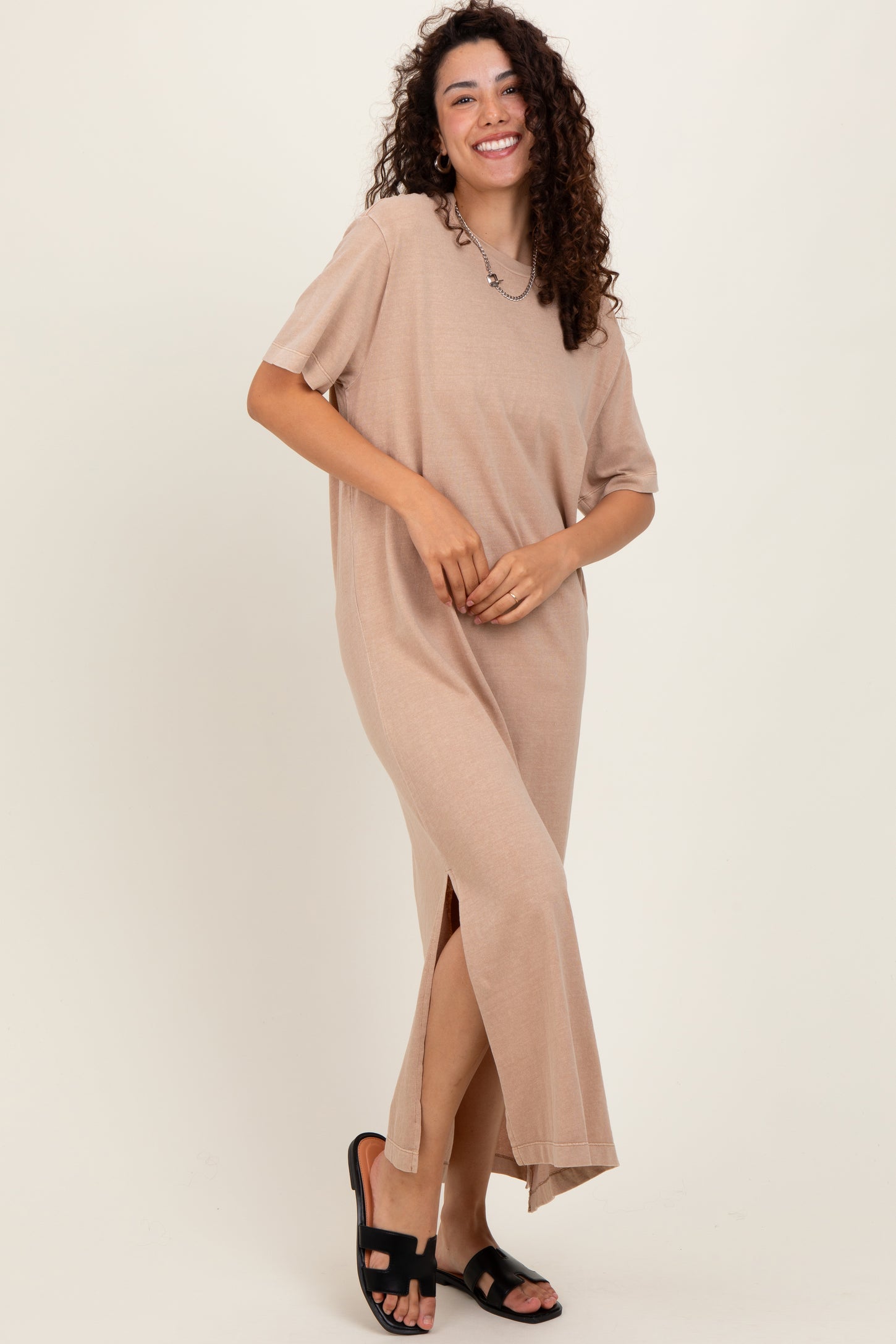 woman wearing a beige short sleeve maxi dress with side slits and standing in black sandals