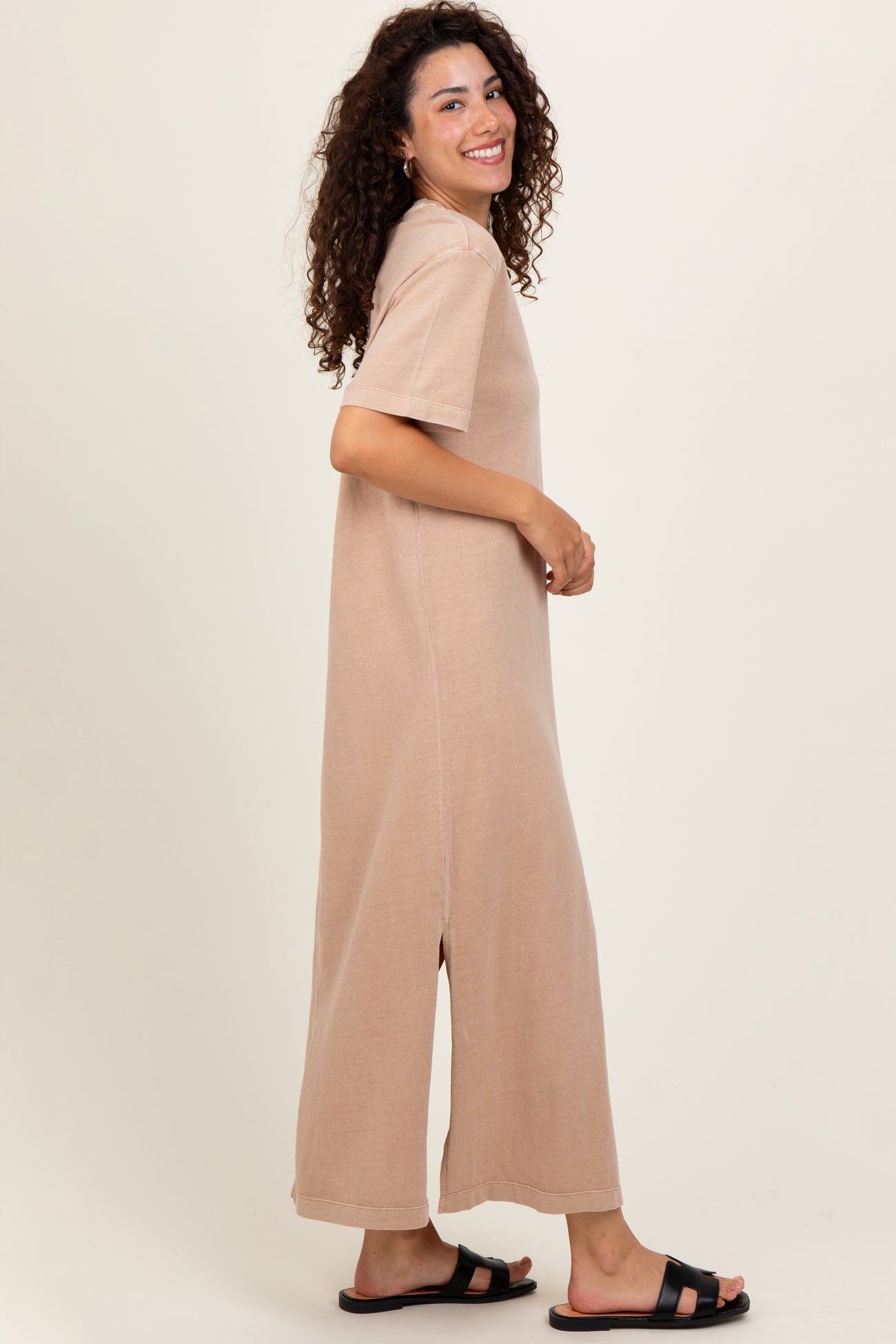 woman wearing a tan short sleeve maxi dress with side slits and black slide sandals