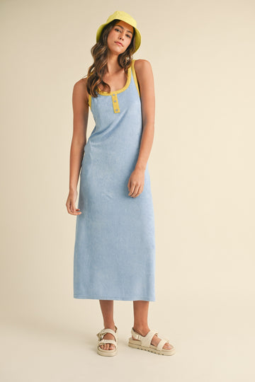 woman wearing a light blue sleeveless maxi dress with yellow straps and buttons, paired with a matching yellow bucket hat