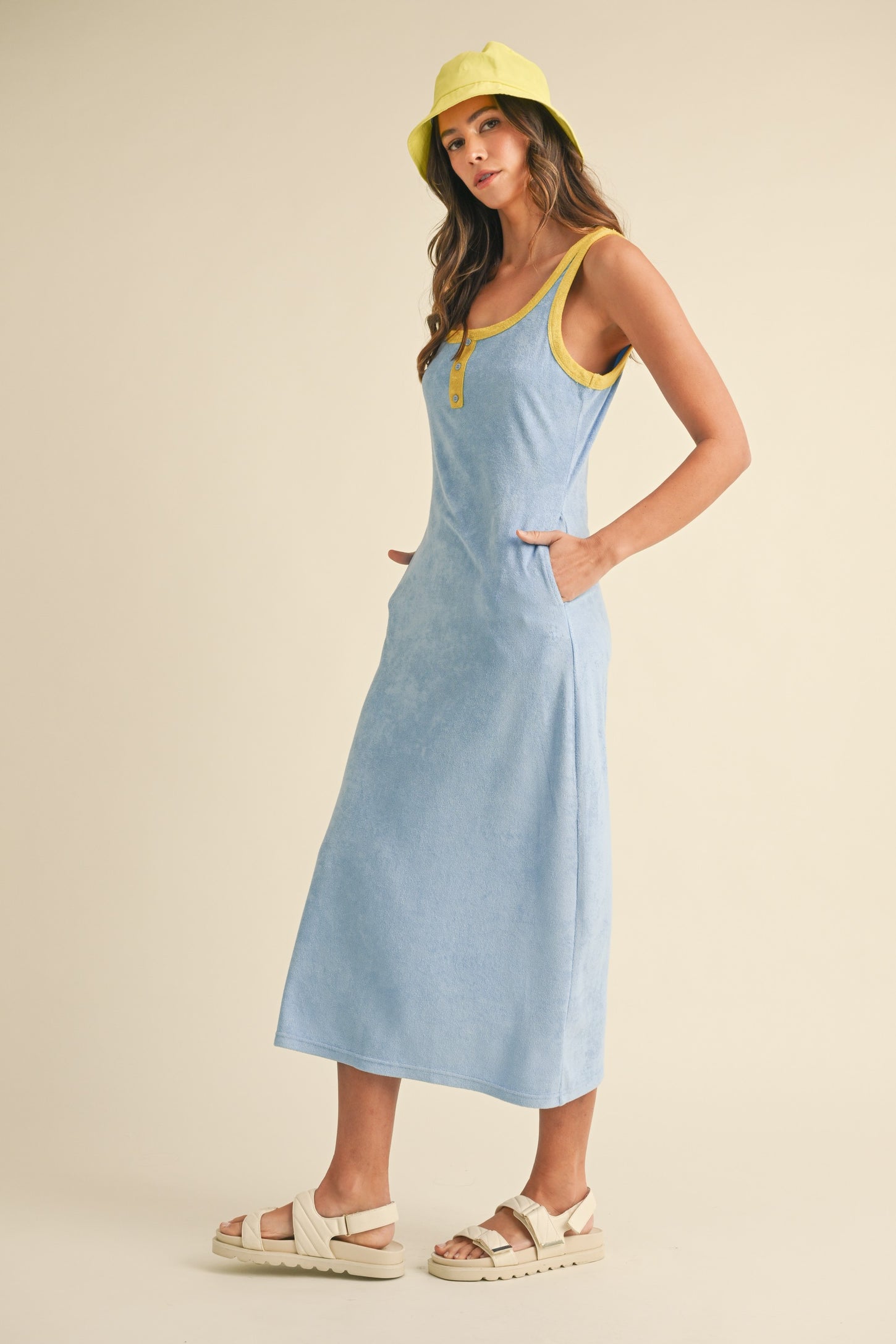 woman wearing a light blue sleeveless maxi dress with yellow trim and pockets, paired with a yellow bucket hat
