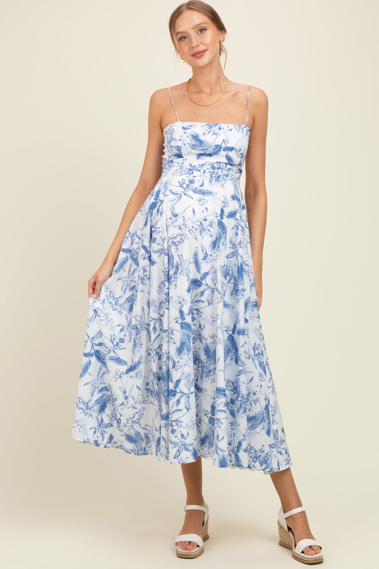 woman wearing a blue floral maternity dress with spaghetti straps and a flowing skirt, showcasing her baby bump