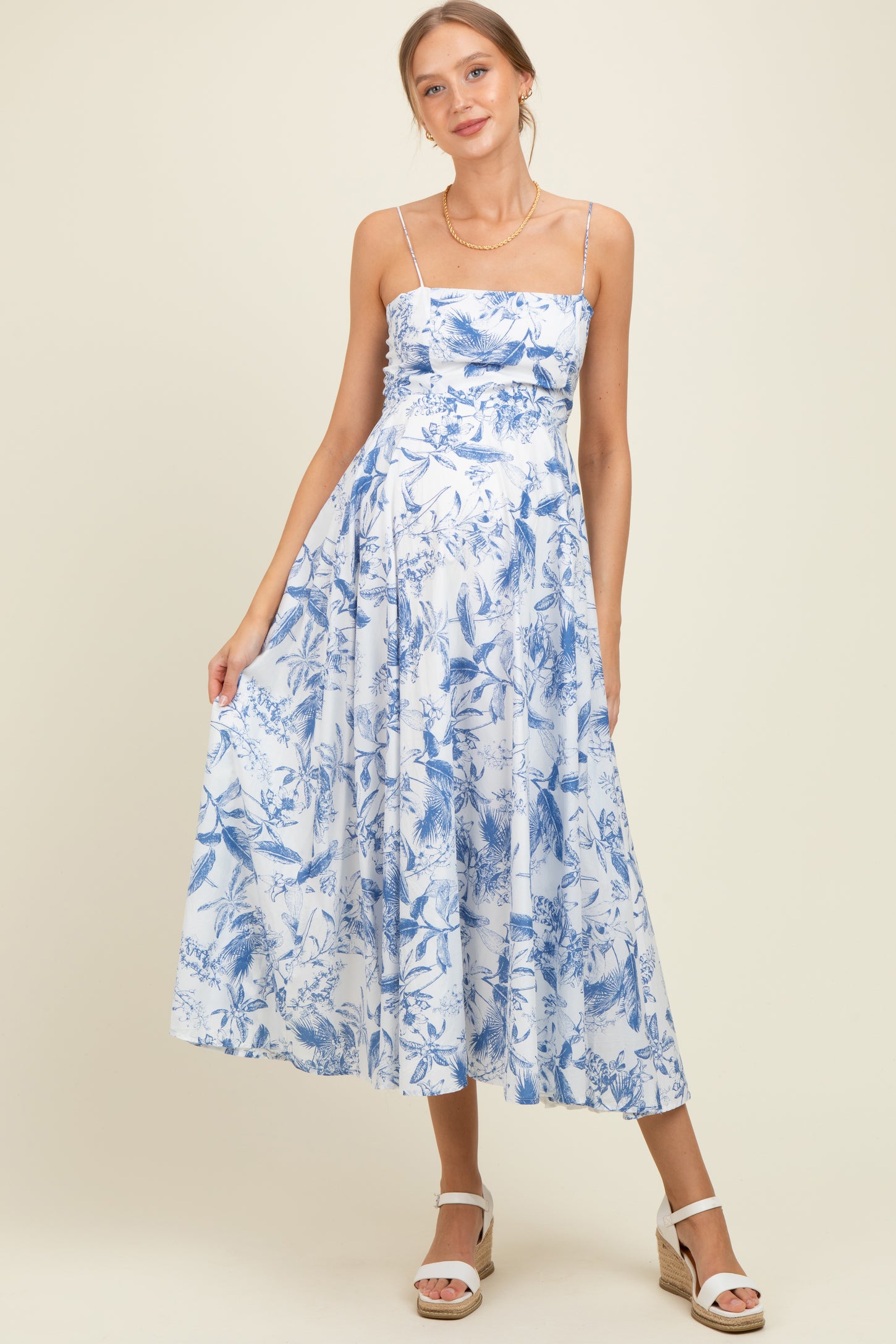 woman wearing a blue floral maternity dress with spaghetti straps and a flowing skirt, showcasing her baby bump