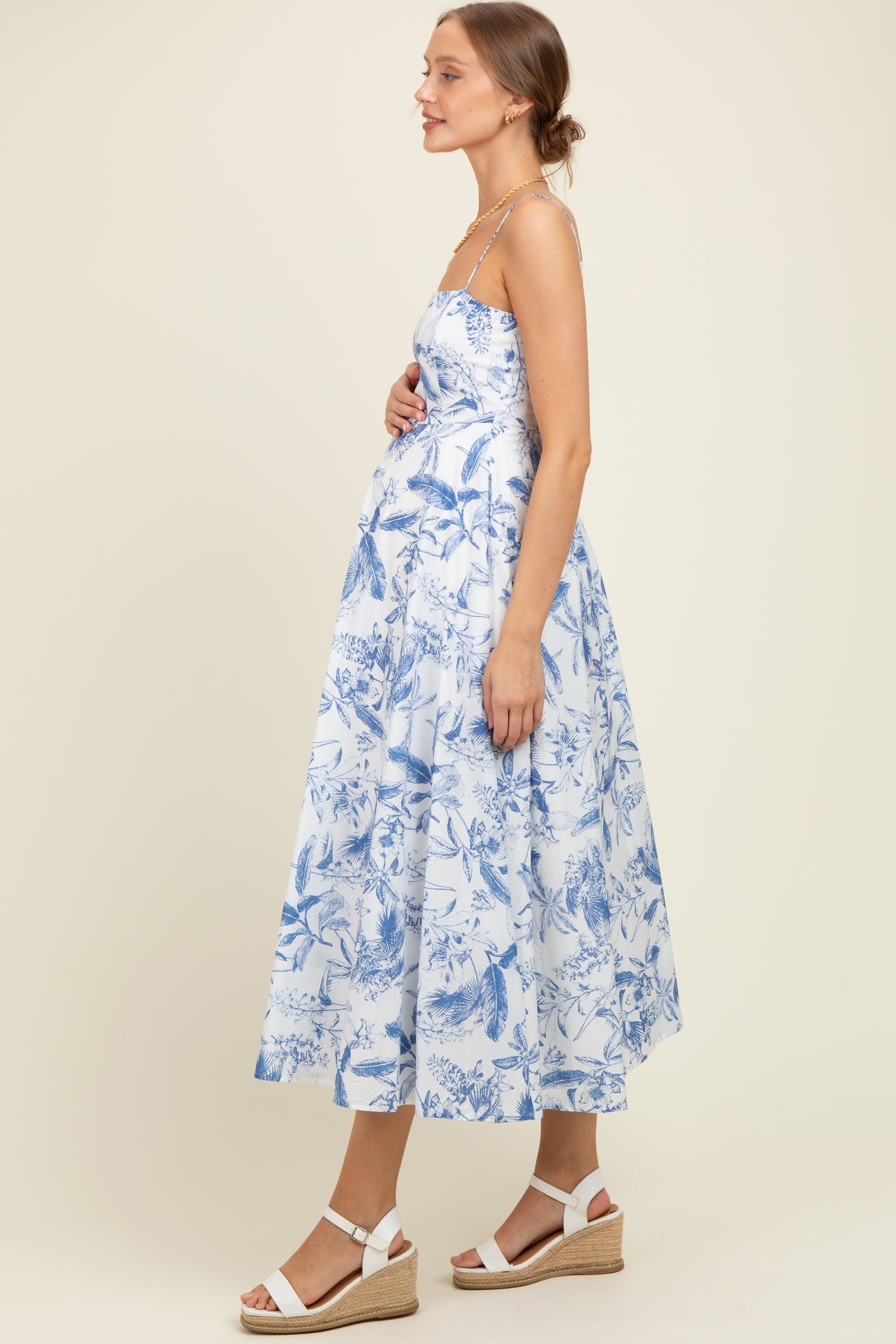 woman wearing a blue and white floral print maternity dress with a flowy skirt and holding her baby bump