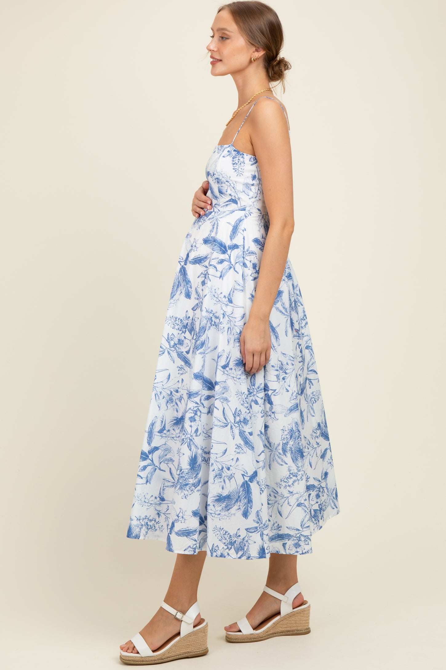 woman wearing a blue and white floral print maternity dress with a flowy skirt and holding her baby bump