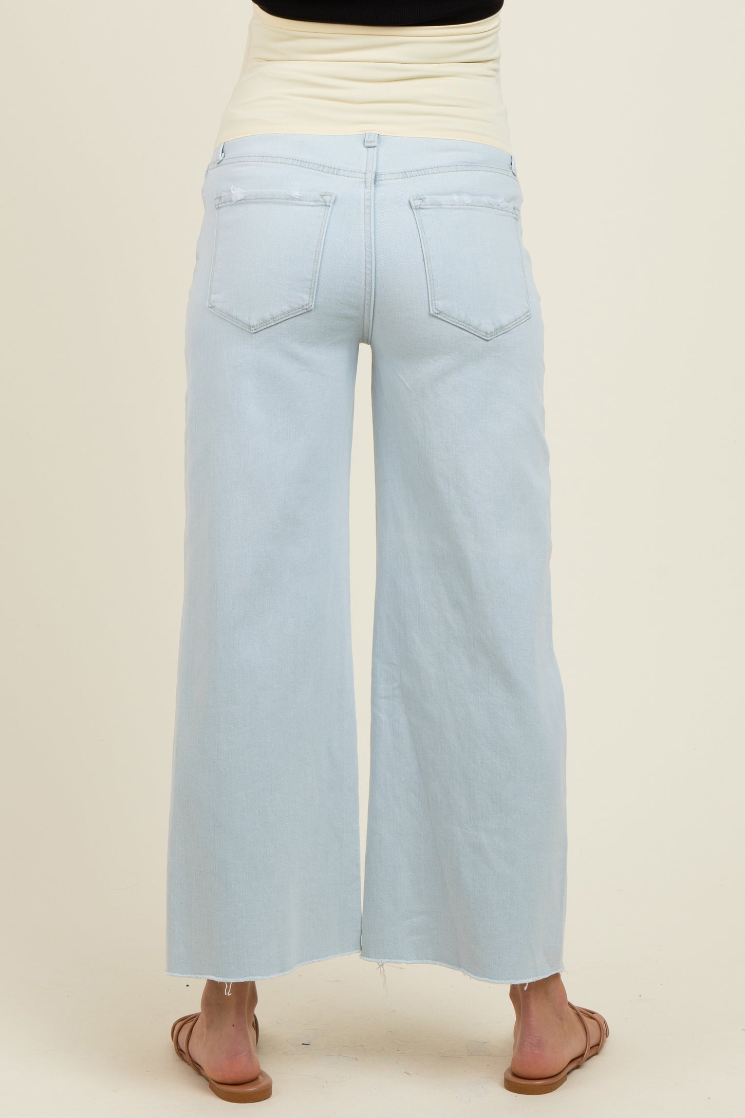 woman wearing light blue wide leg maternity jeans, with a fold-over waistband and sandals, view from the back