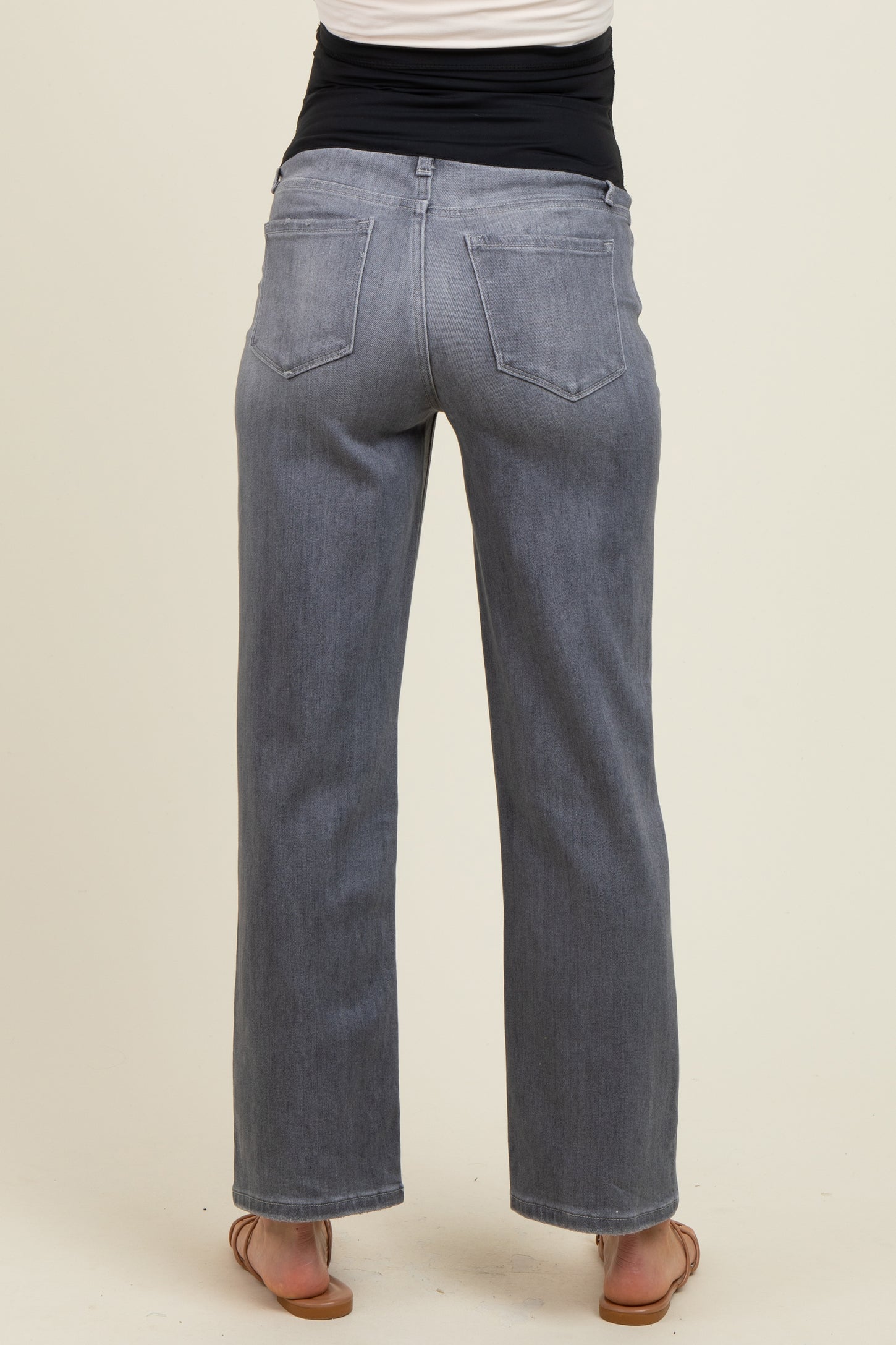 woman wearing grey maternity wide-leg jeans, seen from the back with a black waistband and casual sandals