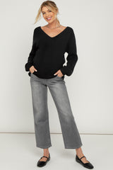 woman wearing a black v-neck oversized maternity sweater and gray wide-leg jeans, showcasing her baby bump