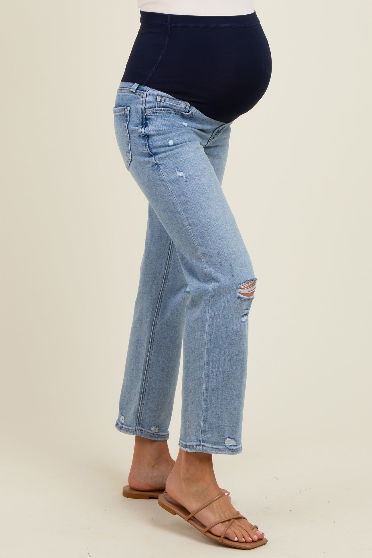 woman wearing light blue maternity jeans with a dark blue over-the-bump panel and distressed details, showing her baby bump