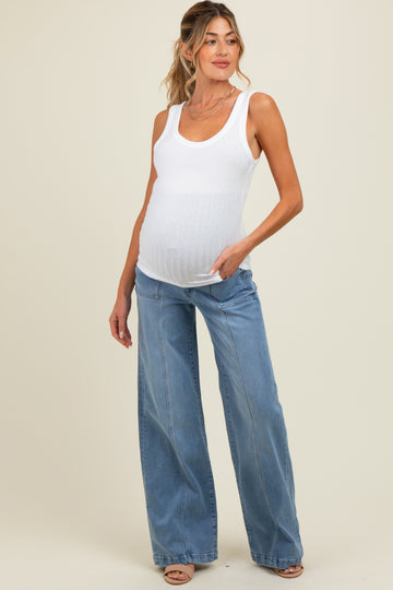 woman wearing a white maternity tank top and high-waisted blue wide-leg jeans, gently holding her baby bump