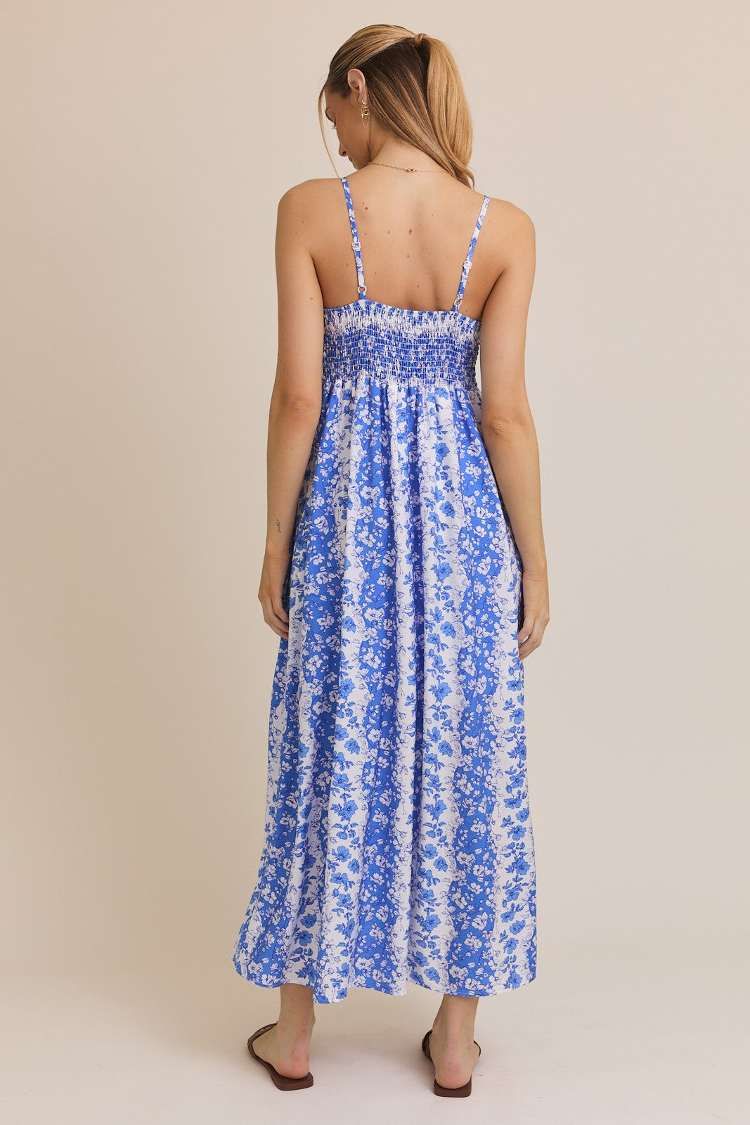 woman wearing a blue and white floral maxi dress with smocked bodice and thin straps, viewed from the back