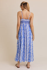 woman wearing a blue and white floral maxi dress with smocked bodice and thin straps, viewed from the back