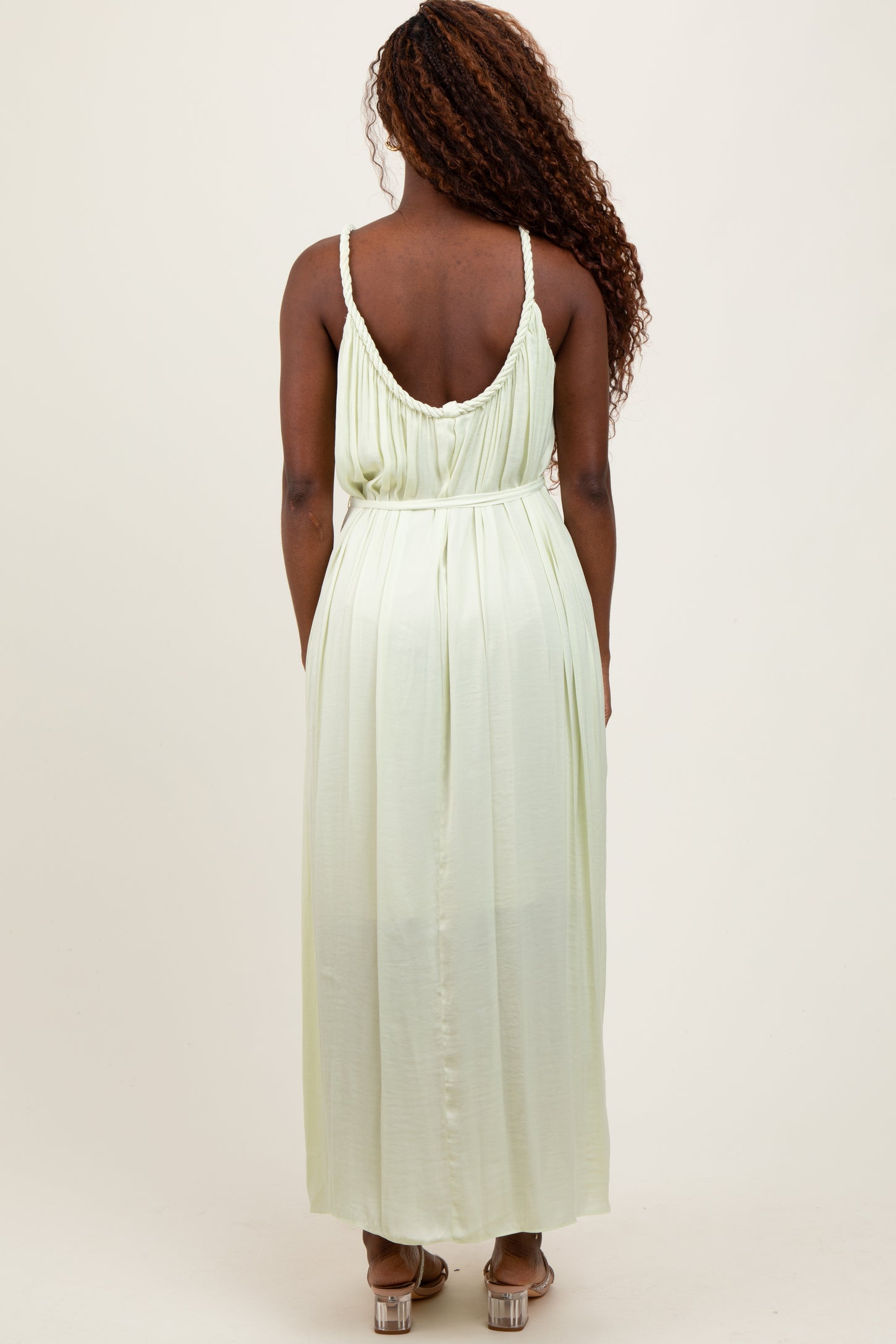 woman wearing a light green maxi dress with a scoop back and braided straps seen from the back