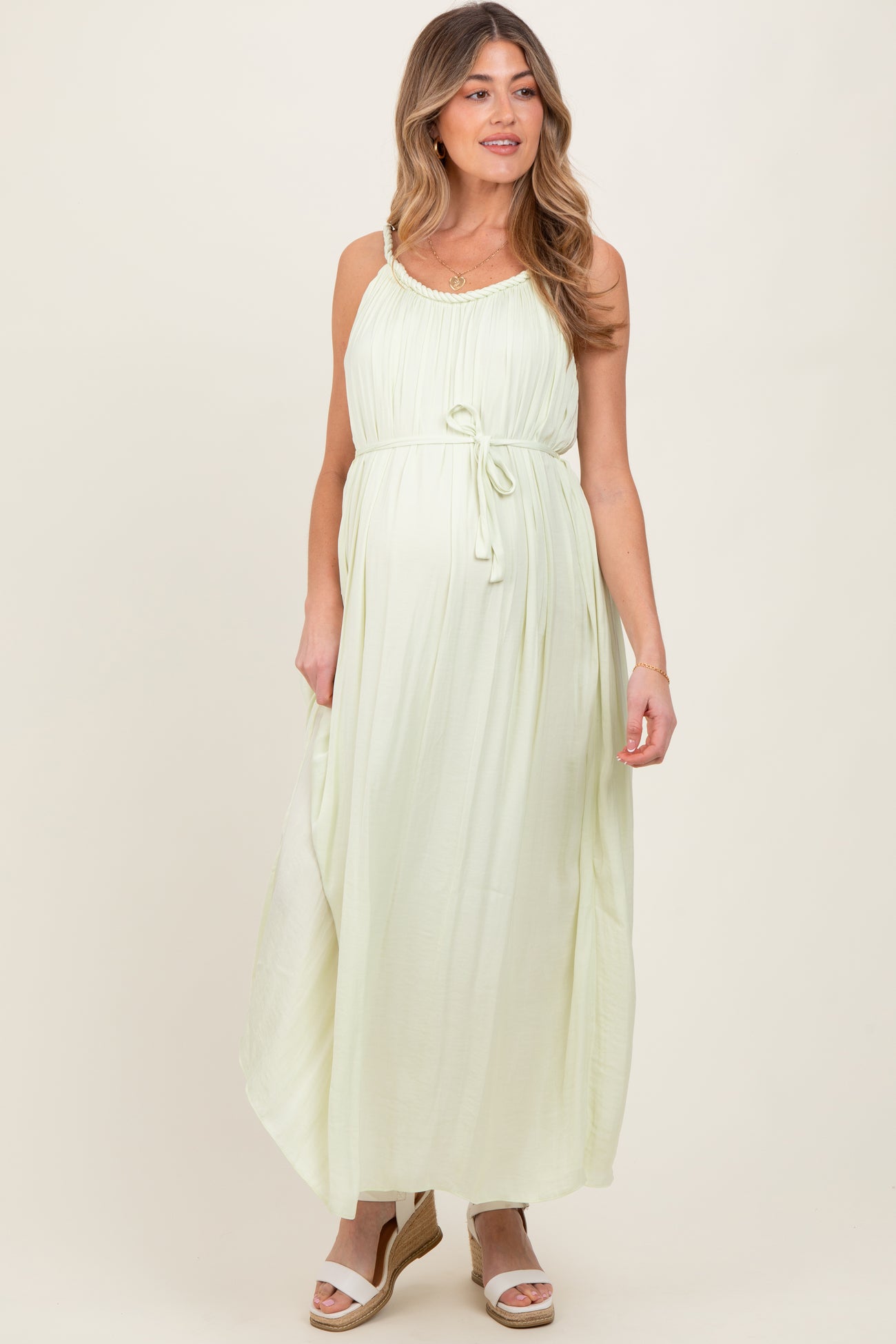 woman wearing a light green maternity maxi dress with a tie waist and adjustable straps, showing a baby bump