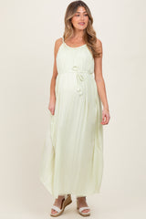 woman wearing a light green maternity maxi dress with a tie waist and adjustable straps, showing a baby bump