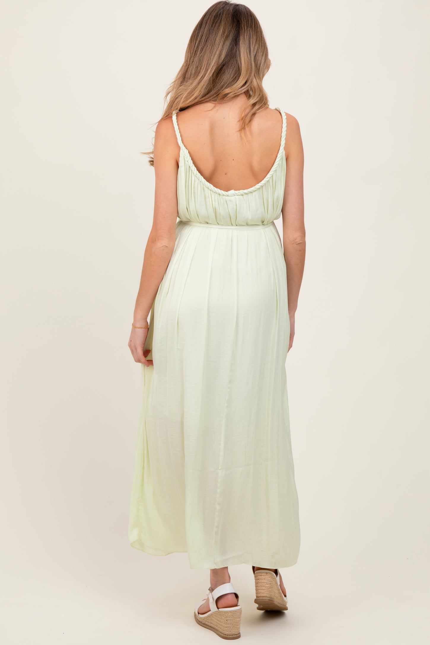 woman wearing a light green maternity maxi dress, showcasing a back view with adjustable straps and a flowy silhouette