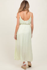 woman wearing a light green maternity maxi dress, showcasing a back view with adjustable straps and a flowy silhouette