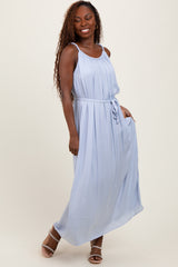 woman wearing a light blue sleeveless maxi dress with a tie belt and pleated details