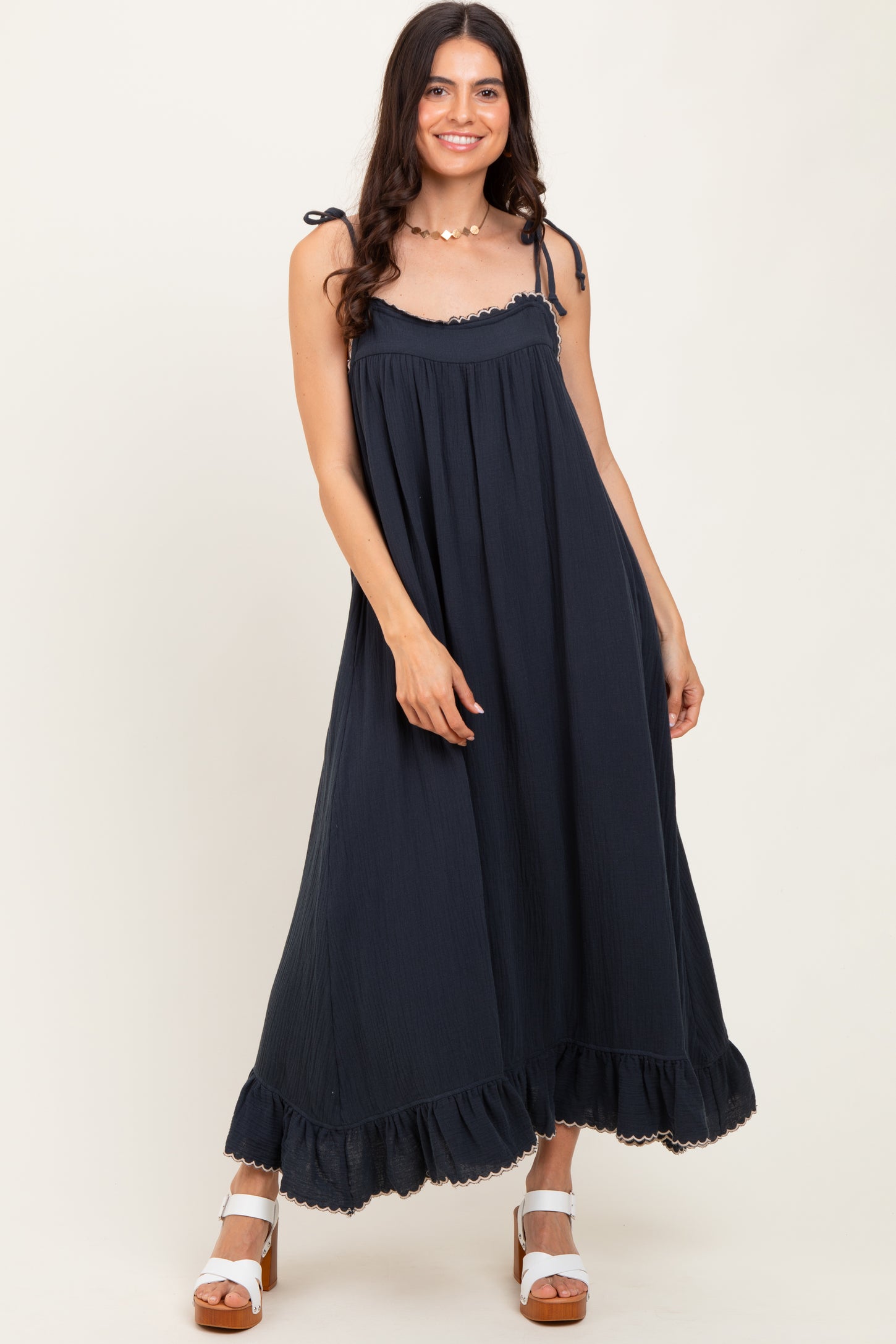 woman wearing a navy blue maxi dress with adjustable straps and a ruffled hem, standing and smiling